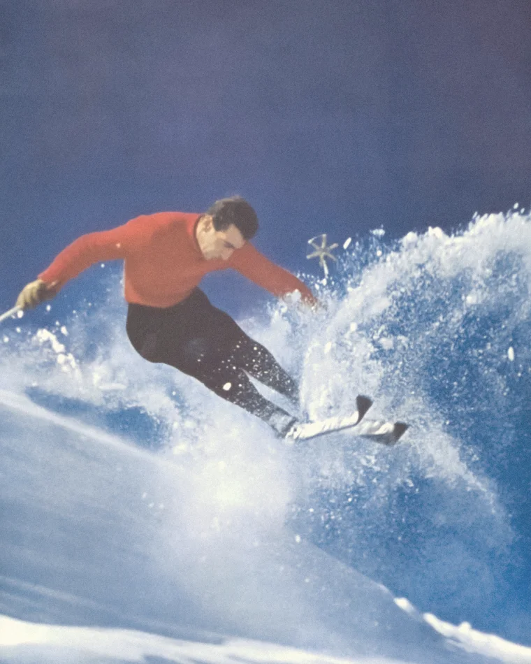 A skier in a red sweater carving hard, throwing a wall of snow