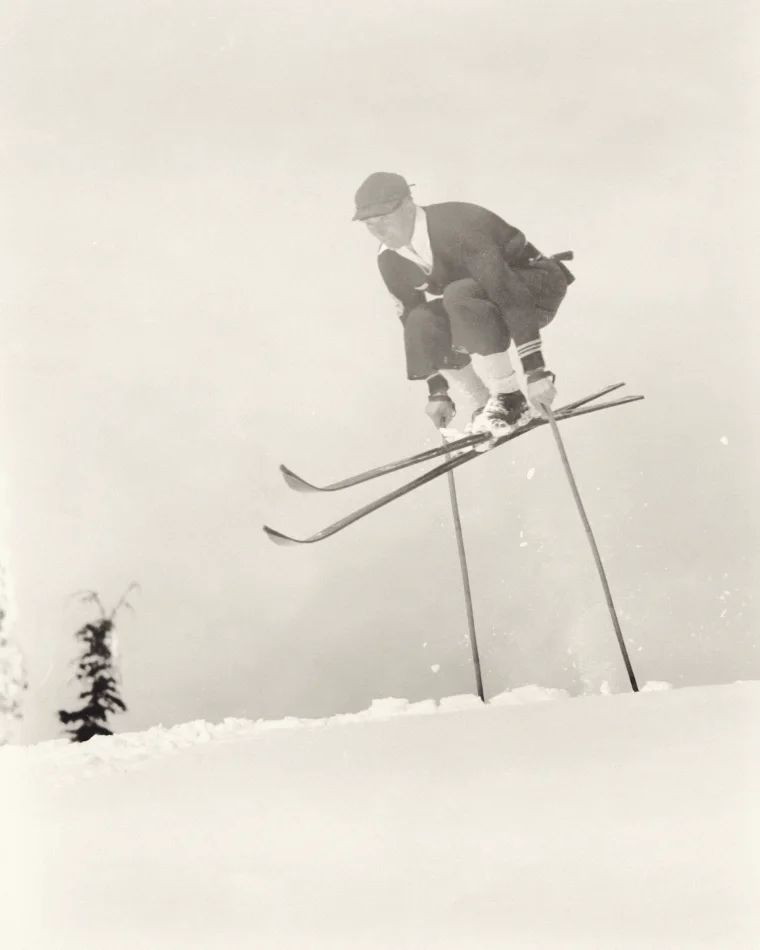 A ski jumper mid-flight against an open white sky