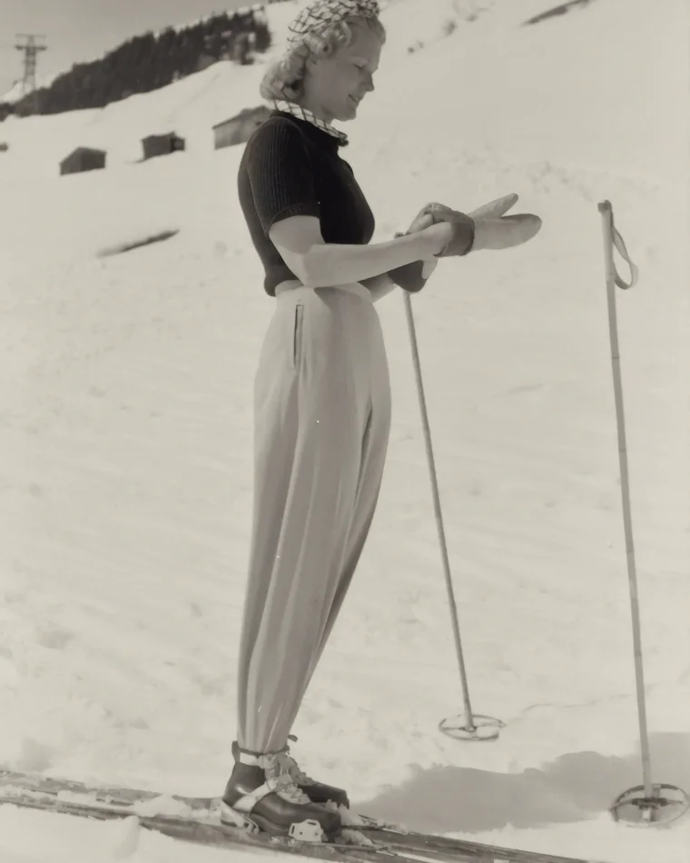 A skier in knitted top and wide trousers pauses on a snow slope, 1930s